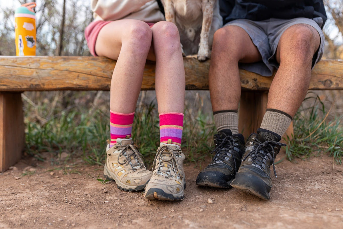 two people sitting on wood bench wearing socks with hiking boots