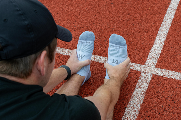 man stretching on a running track while wearing grey socks