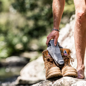 Person holding hiking boots and socks outdoors near a natural setting