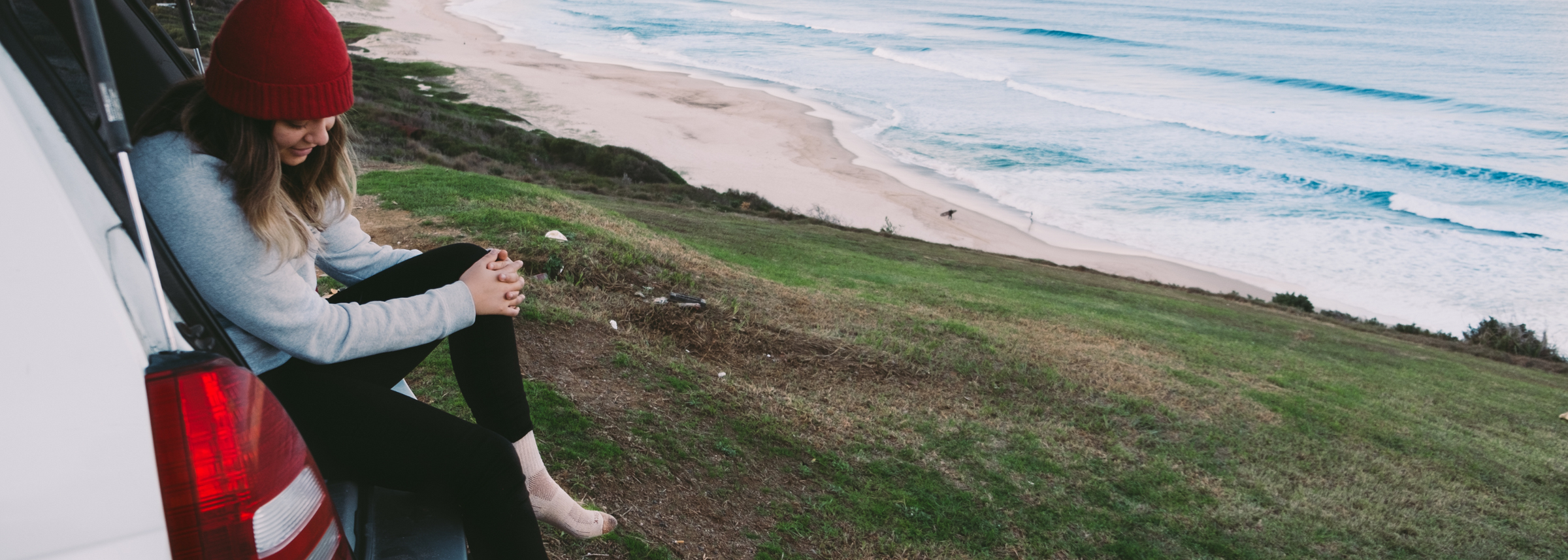 person wearing tan sock sitting in trunk of car overlooking ocean cliff